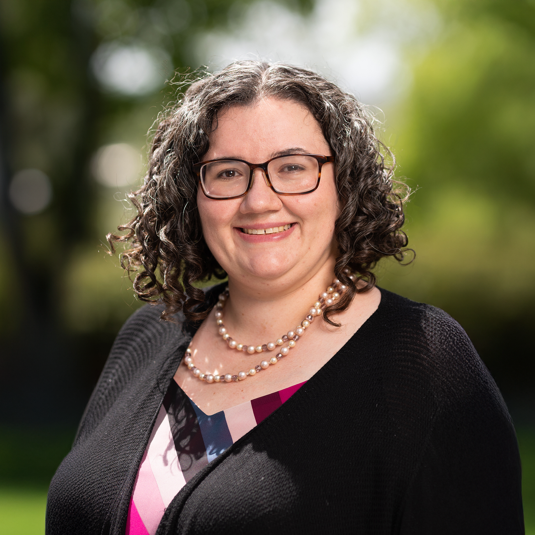 portrait of Jennifer with shoulder length curly hair, smiling and wearing glasses